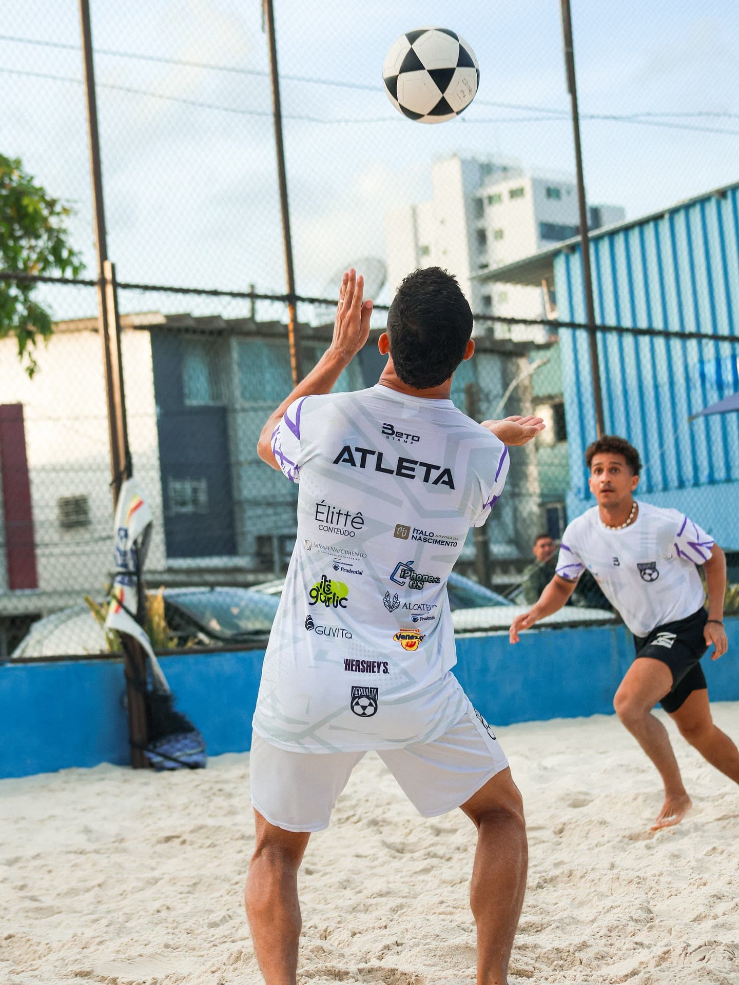 Atleta de camisa branca do Aero Alta 81 preparando o voleio com a bola no alto, na areia