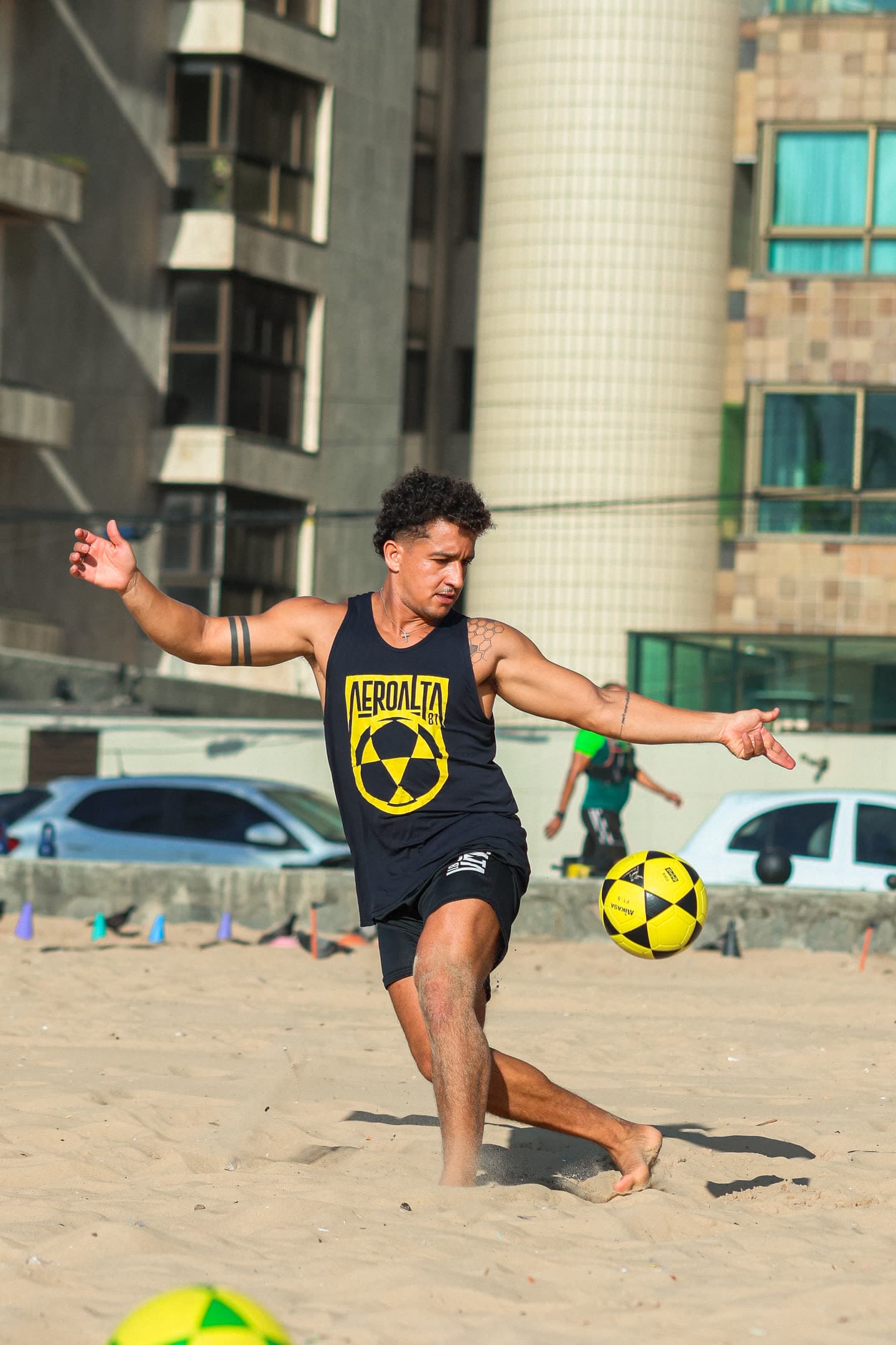 Atleta de regata preta com o escudo amarelo do Aero Alta 81 chutando a bola na areia