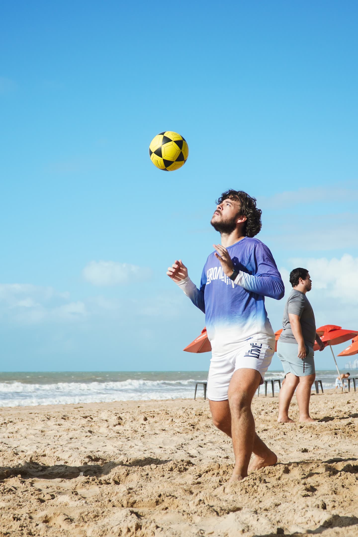 Atleta de manga longa do Aero Alta 81 esperando a bola descer para dominar, com o mar ao fundo