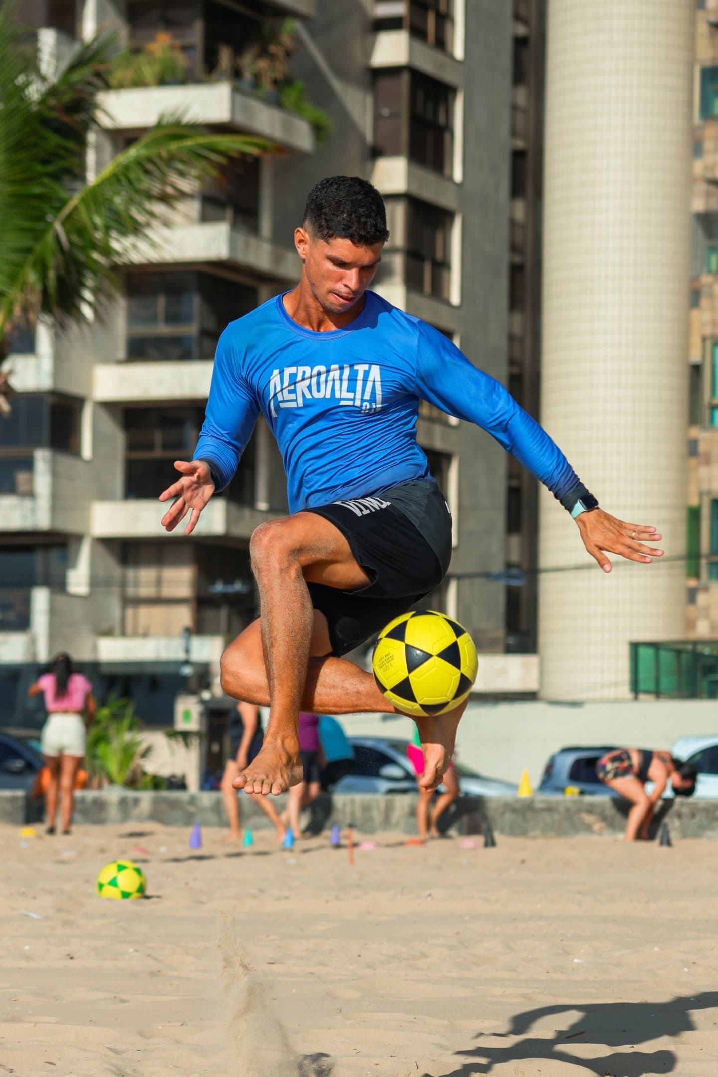 Atleta de camisa azul do Aero Alta 81 suspenso no ar dominando a bola com a coxa, coqueiro ao fundo
